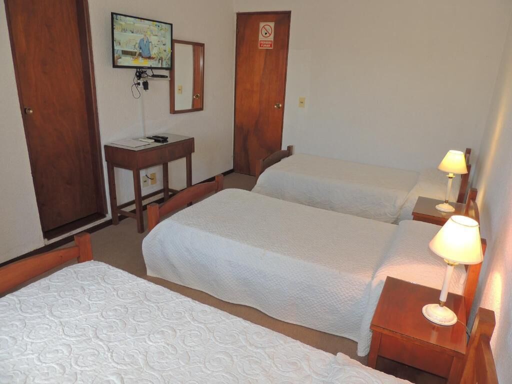 A hotel room with two beds, a desk with a chair, a television, and a lamp.