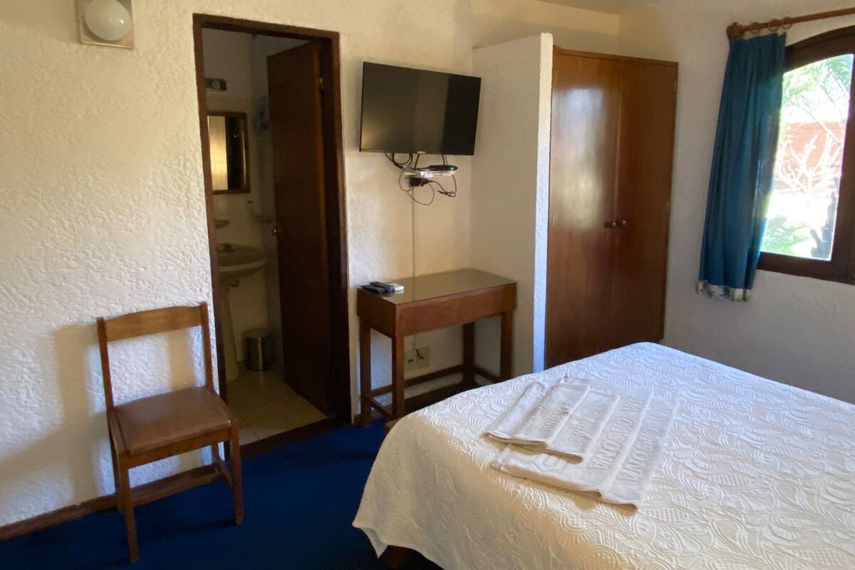 Un dormitorio con cama, escritorio, silla, ventilador de techo y televisor.
