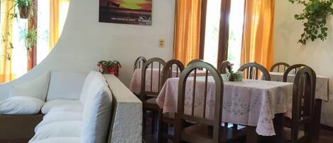 A dining area with a sofa, dining tables, chairs, and curtains.
