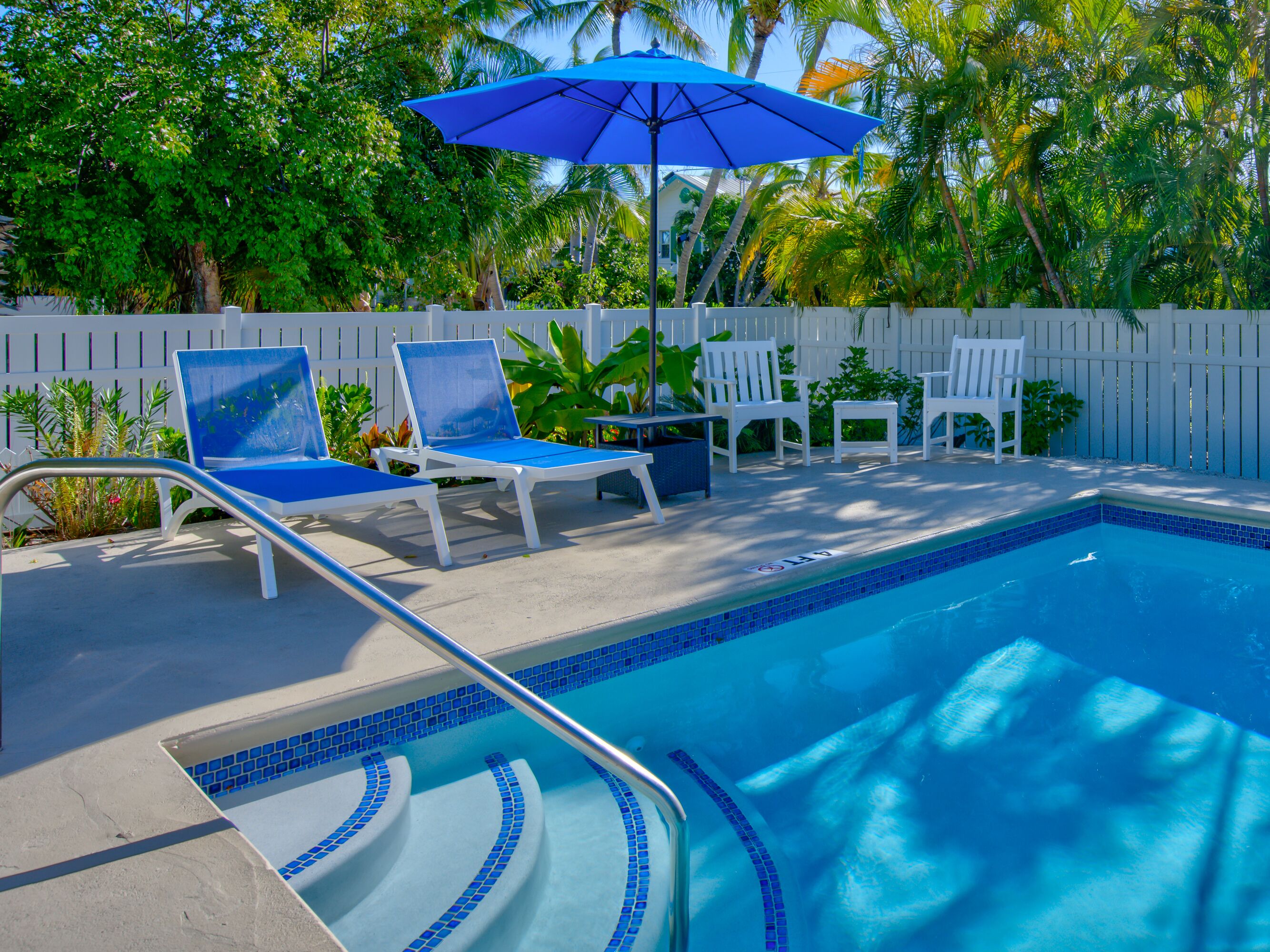 Une piscine avec des marches recouvertes de carreaux bleus, des chaises longues blanches et un parasol bleu.
