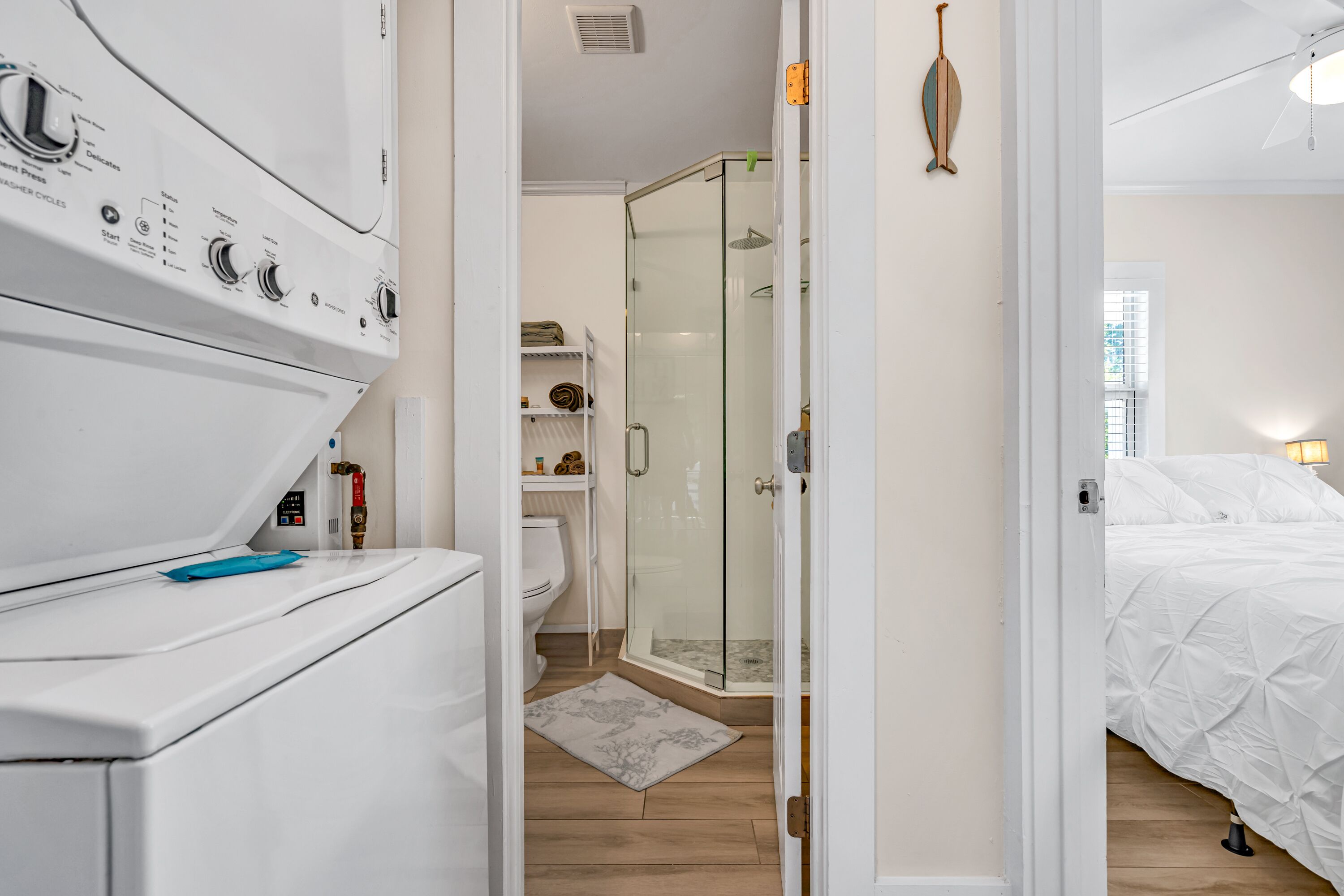 A laundry area with a washing machine, a glass shower enclosure, and a bed with white bedding.