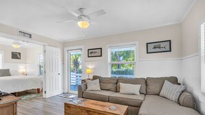 A spacious living room with a large sofa, a wooden coffee table, and a ceiling fan. There are two doors leading to other rooms, and the walls are painted in a light color. - Bungalow #4 - 2 Bed/1 Bath & Pool in Islamorada (Islamorada)