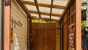 A wooden shed with a metal roof, a door with a decorative shell hanging, and a small step leading into the shed.
