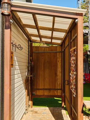 A wooden shed with a metal roof, a door with a decorative shell hanging, and a small step leading into the shed.
