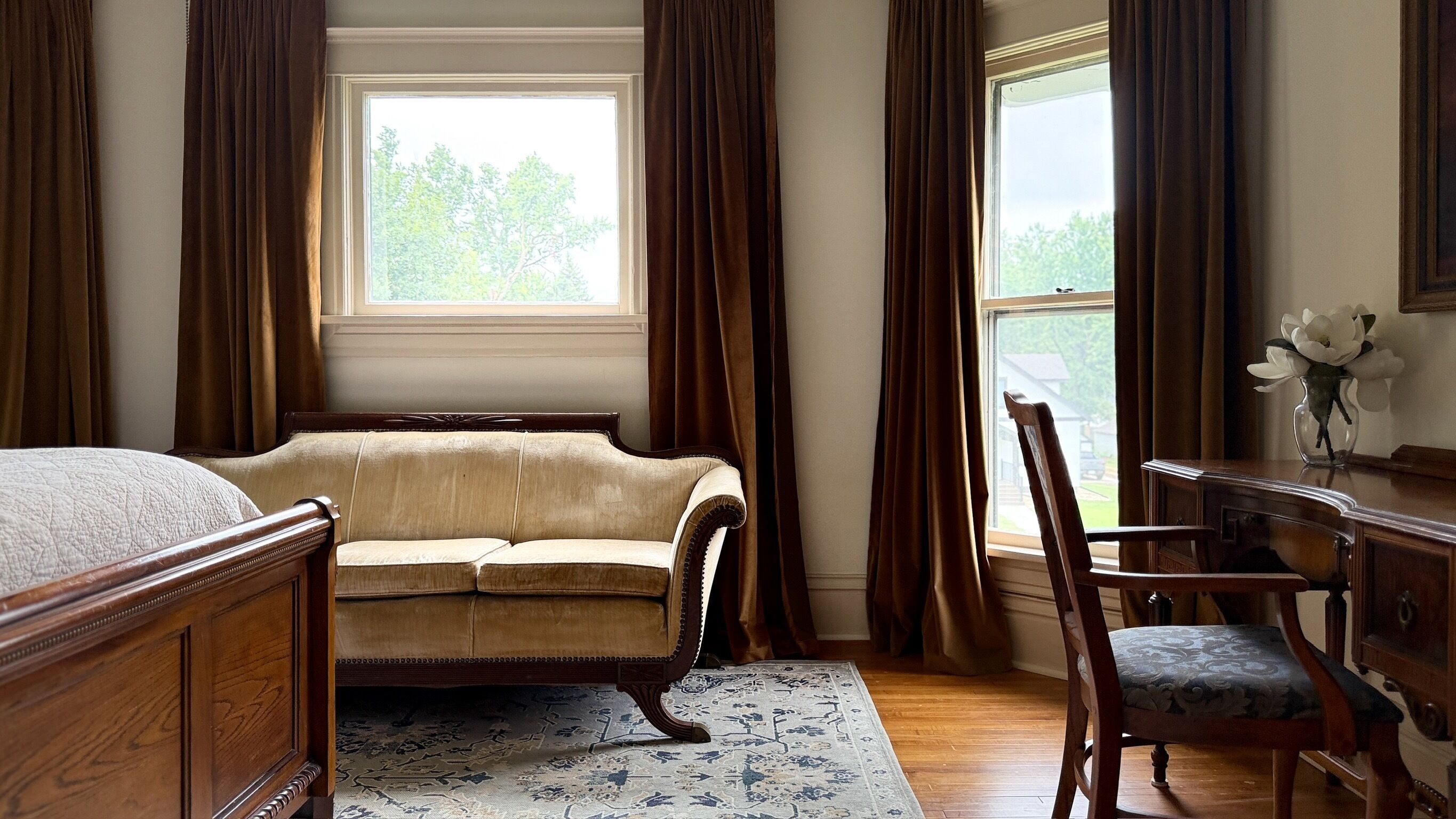 A room with a bed, a sofa, a chair, a desk, and a window with curtains.