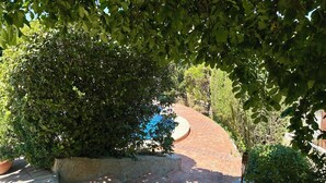 A paved courtyard with a circular brick feature, surrounded by dense foliage and a stone wall. - Rural house El Arado (Baena)