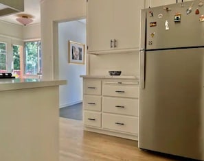 Eine Küche mit einem Edelstahl-Kühlschrank, weißen Schränken und einer kleinen Kochinsel mit einer Schüssel.