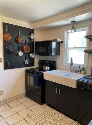 Compact kitchen with black stove, sink, and microwave, offering ample storage and a tiled floor.