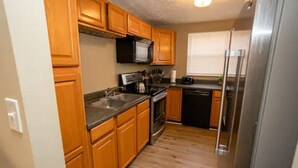 A compact kitchen with wooden cabinets, a stainless steel refrigerator, and a microwave. - Tollgate · 7602 Tollgate Ct, Florence (Florence)