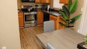 A compact kitchen with wooden cabinets, stainless steel appliances, and a dining area with a table and chairs. - Tollgate · 7602 Tollgate Ct, Florence (Florence)