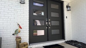 A black double door with multiple panels and a doormat with "hello" on a white brick wall. - Large Remodeled Central Located Minutes to the Beach & Downtown Free Big Parking (Pensacola)