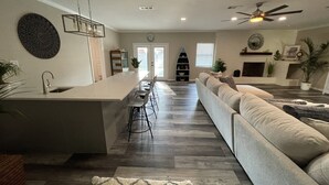 A modern kitchen with a central island, a dining area with bar stools, a large sofa, and a fireplace. - Large Remodeled Central Located Minutes to the Beach & Downtown Free Big Parking (Pensacola)