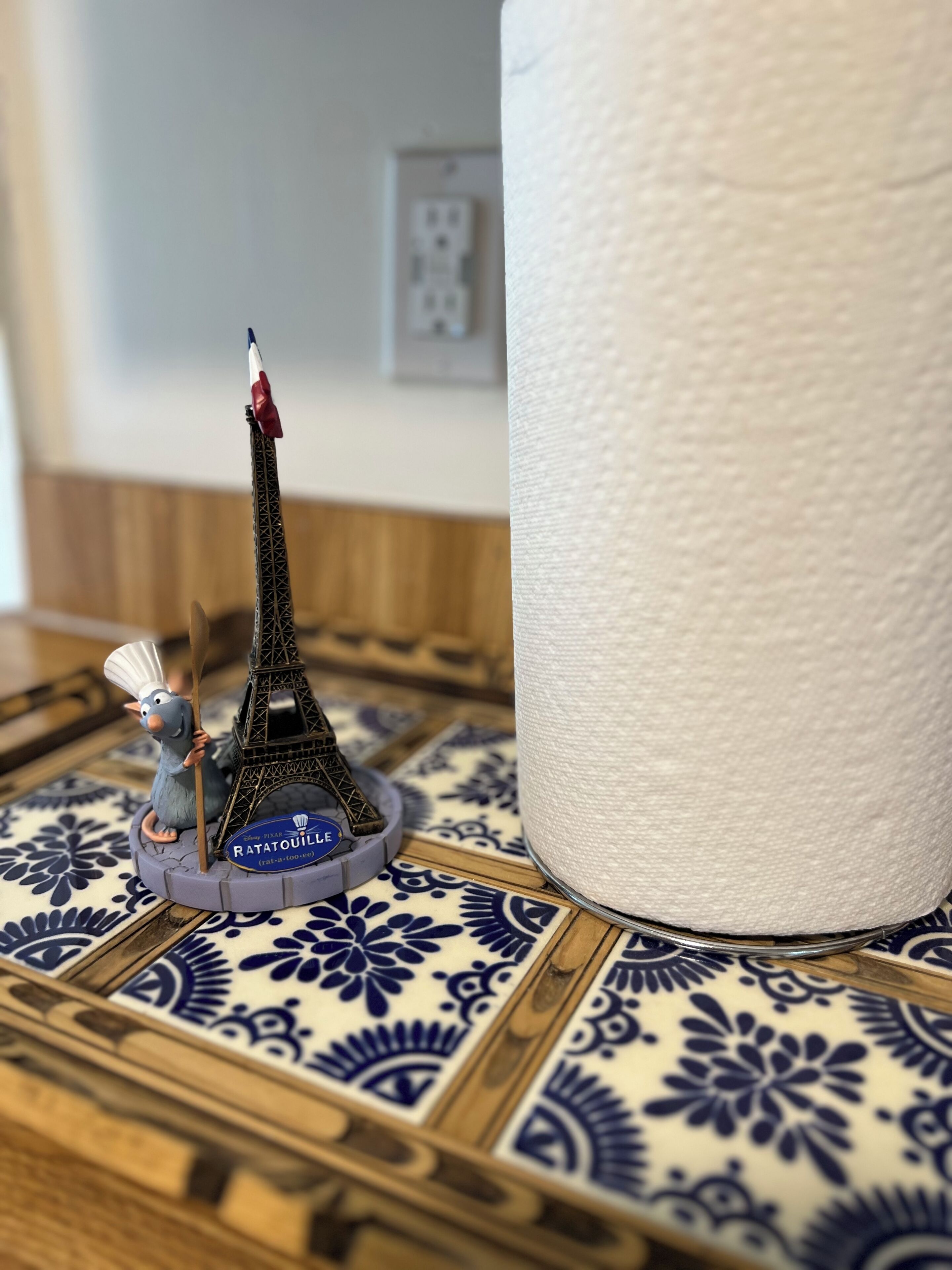 A model of the Eiffel Tower on a decorative tile, a roll of paper towels, and a power outlet in the background.
