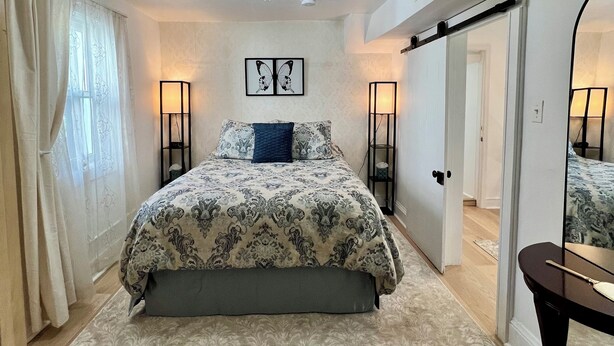 A bedroom with a bed, a chandelier, a mirror, and a door leading to another room. - 1-Min Walk to The Inn • Private Suite, Tub & Full Kitchen. (Washington)