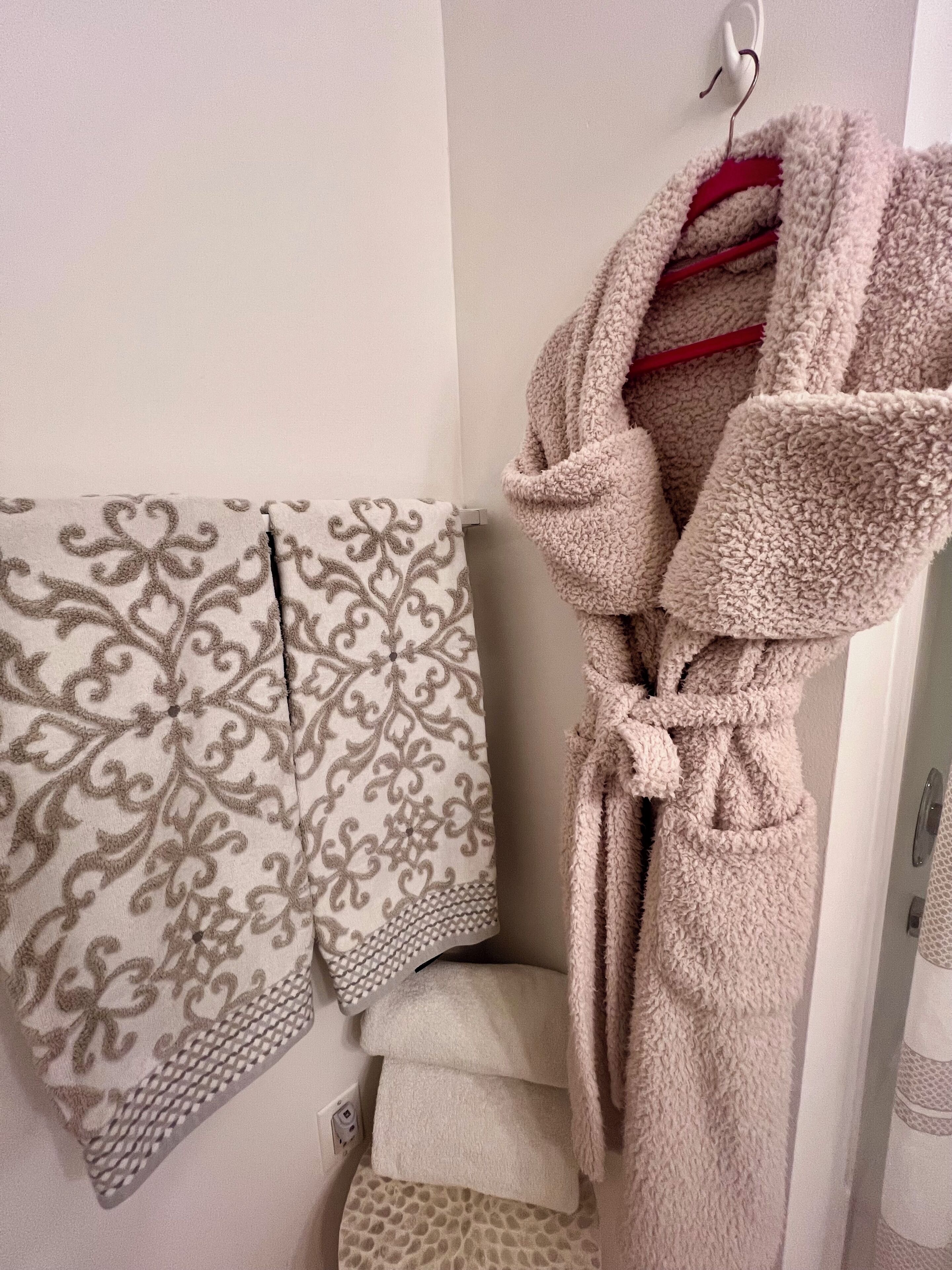 A bathroom with a towel rack holding patterned towels and a fluffy bathrobe.