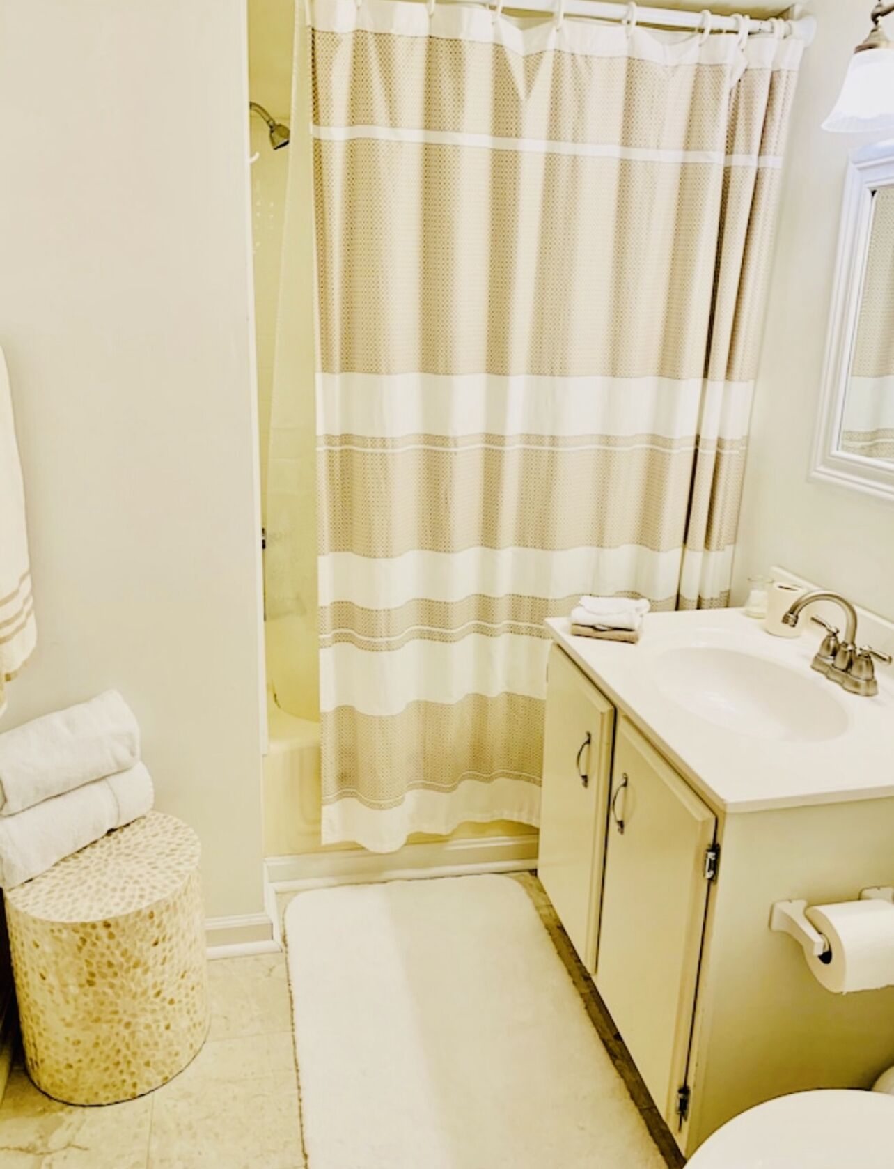 A bathroom with a shower curtain, a sink, a toilet, and a small round stool.
