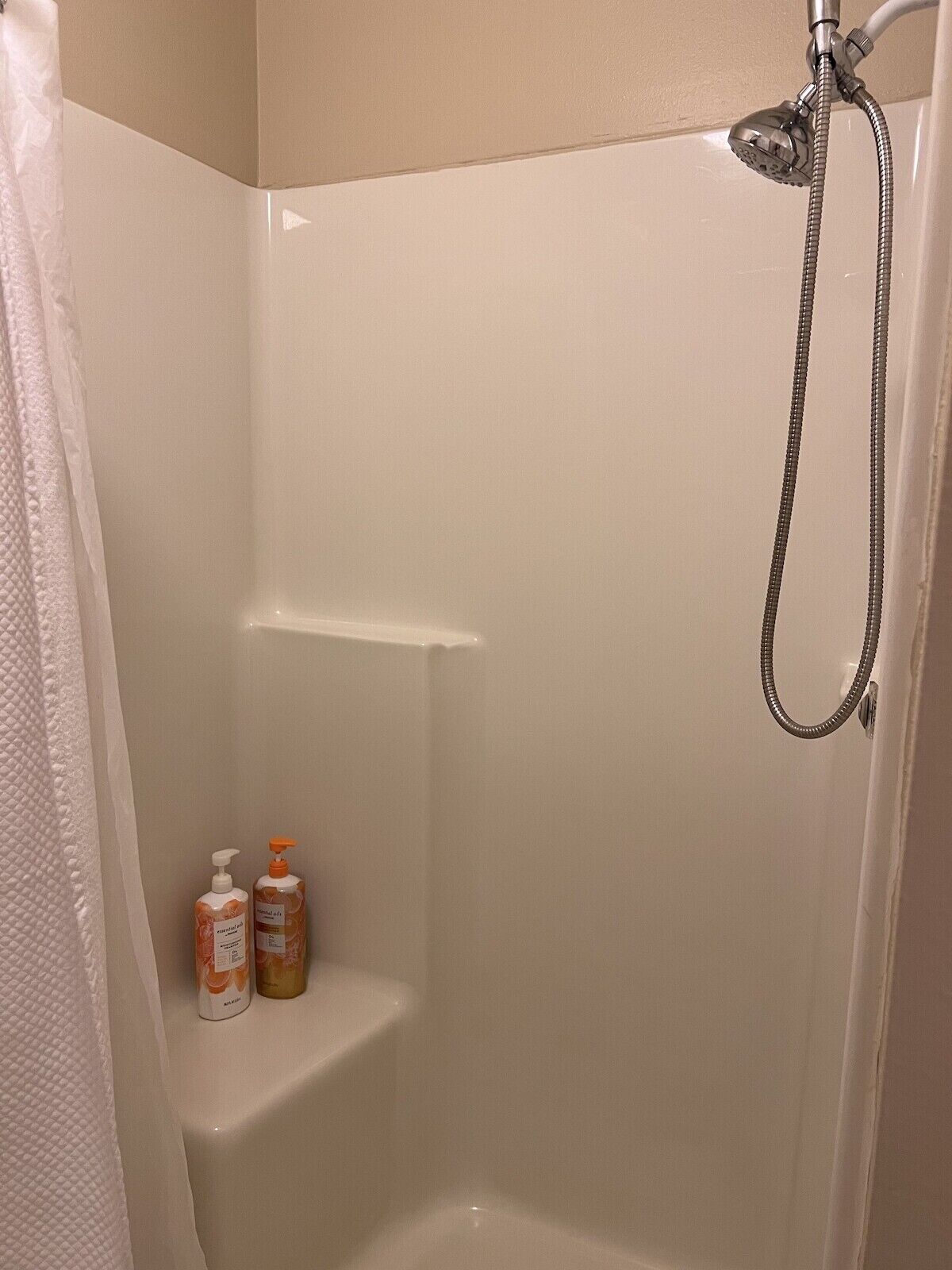 Een douchegedeelte met een handdouche en een in de wand geïntegreerde douchekop. Op een plank staan twee flessen shampoo en conditioner.
