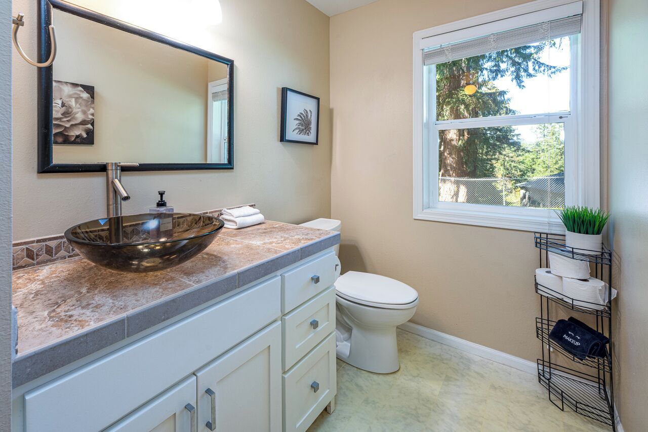 A bathroom with a glass bowl sink, white toilet, and a window with a view of trees.