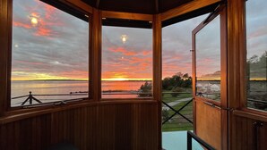 A wooden cabin with large windows overlooking a sunset over a body of water. - Iconic Bristol Ferry Lighthouse (Bristol)