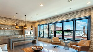 A modern kitchen with a brick wall, large windows, and a dining area with leather chairs and a wooden table.
