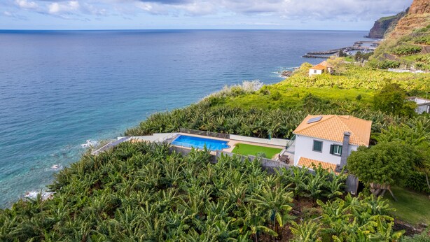 Una proprietà costiera con piscina, verdeggiante vegetazione e vista sul mare.