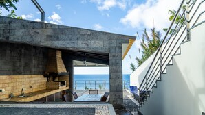 Un'area cucina esterna moderna con vista sul mare, un sentiero in pietra e una scala che conduce a un edificio bianco.