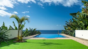Una piscina con vista sull'oceano, circondata da una vegetazione rigogliosa e un cielo azzurro limpido.