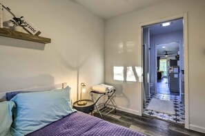 A bedroom with a bed, a bedside table with a lamp, a shelf with a plant, and a door leading to a hallway. - Canyon Lake Retreat w/ Pool ~ 2 Mi to Lake (Canyon Lake)