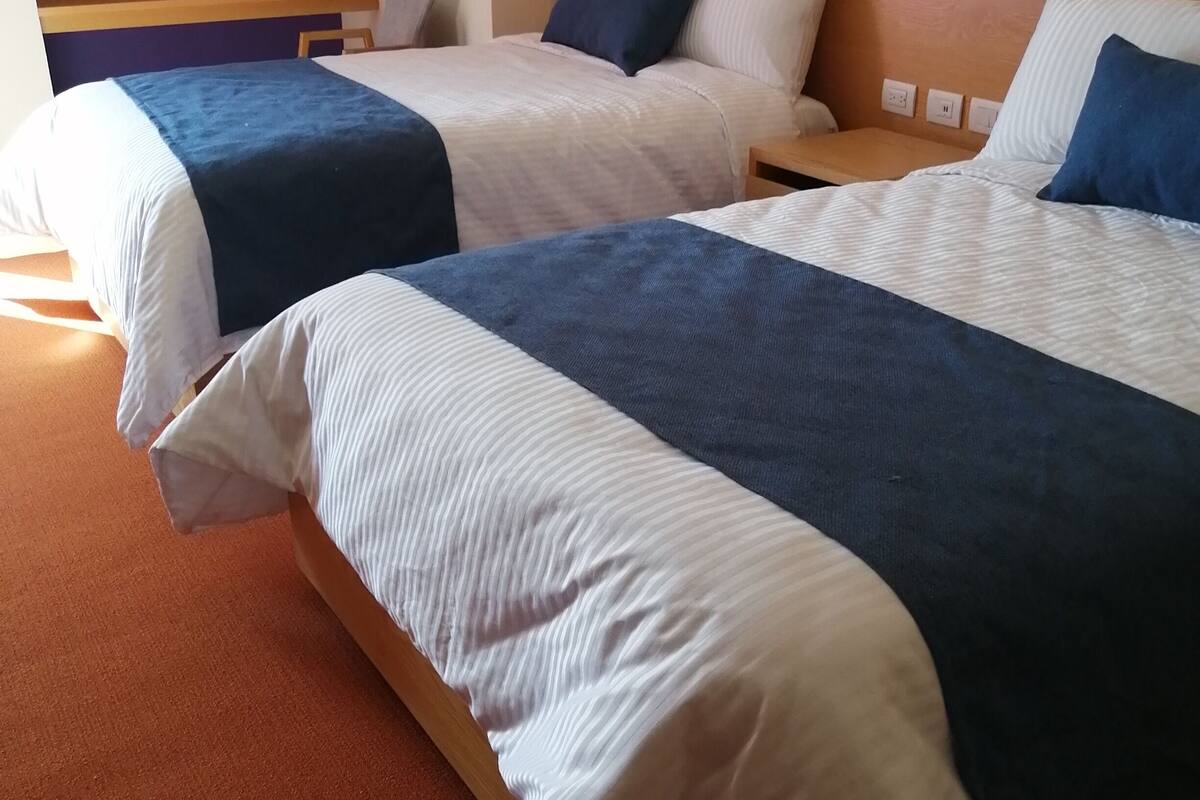 Twee eenpersoonsbedden met houten hoofdborden, een houten nachtkastje en een wandcontactdoos.