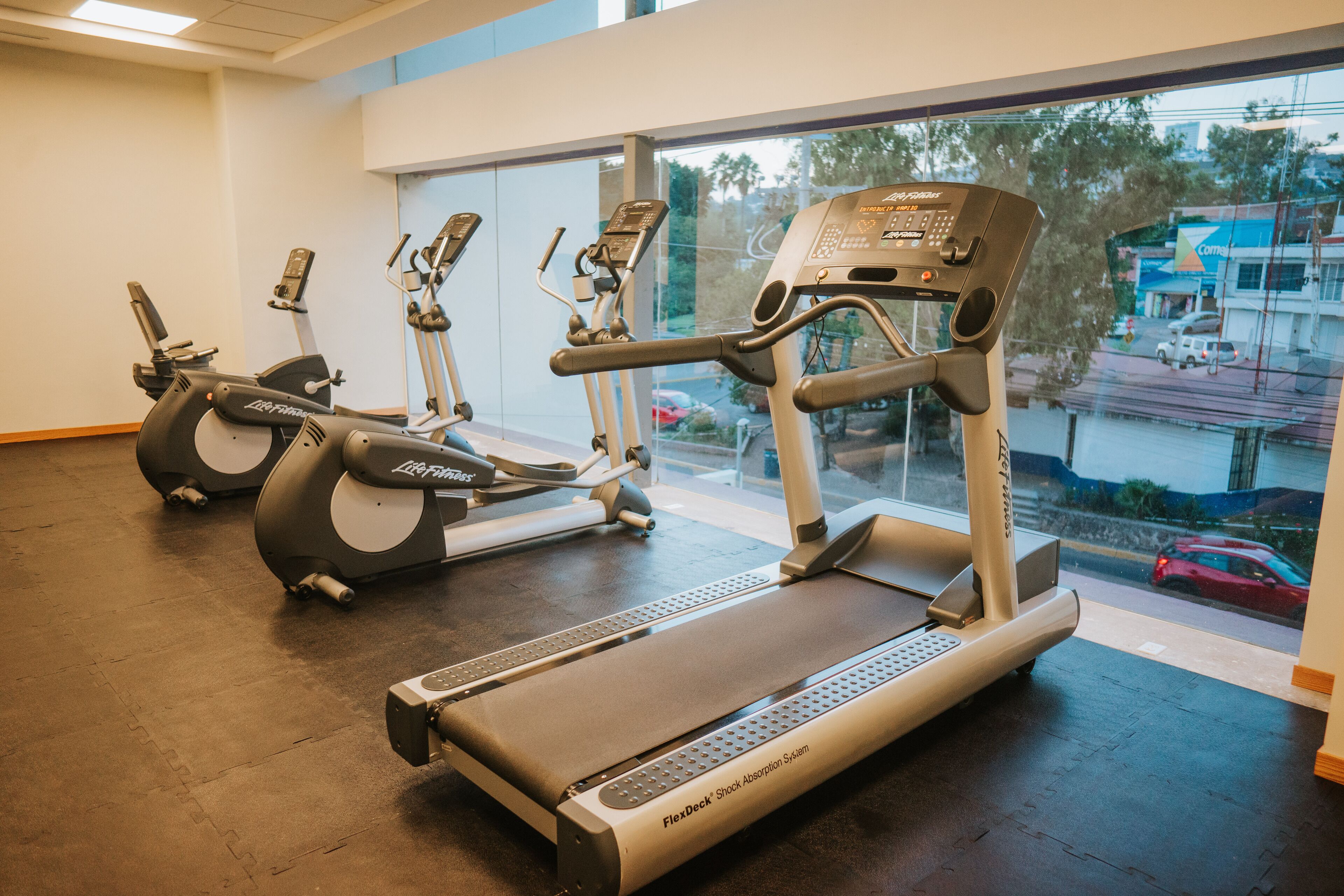 Un gimnasio con cintas de correr, elípticas y un espejo grande.