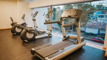 Un gimnasio con cintas de correr, elípticas y un espejo grande.