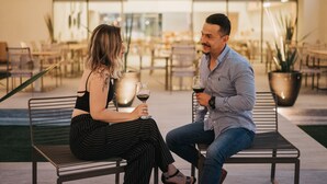 Two people sitting on a bench outdoors, holding wine glasses.