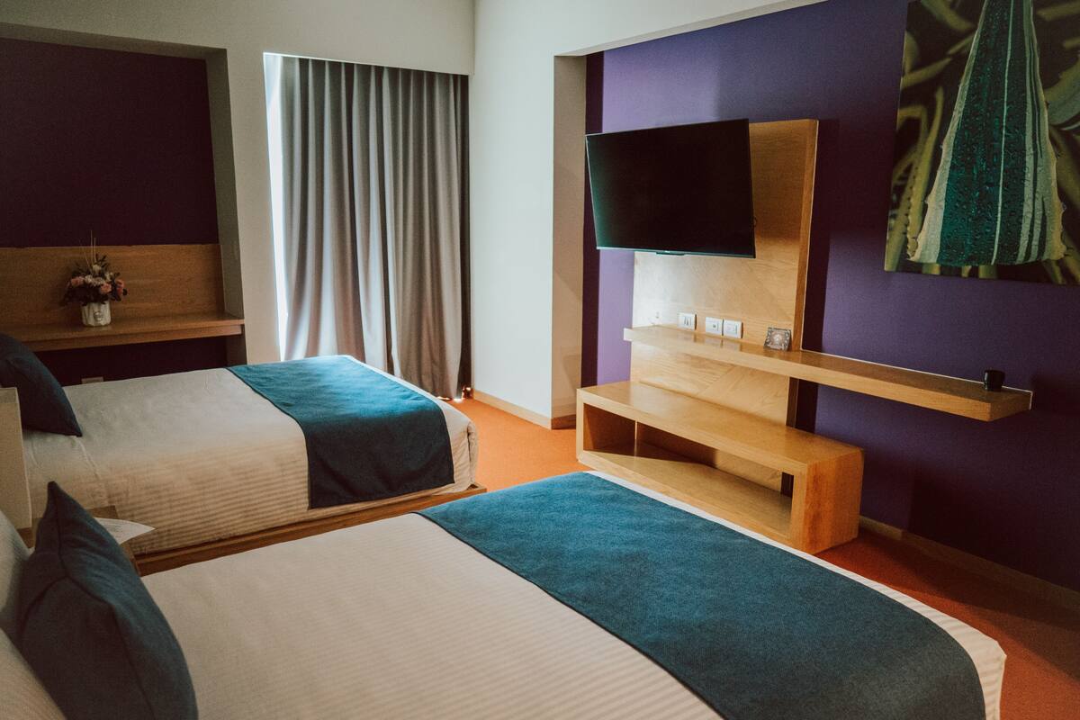 Een hotelkamer met twee bedden, een flatscreen televisie bevestigd aan een houten plank, en een groot schilderij aan de muur.
