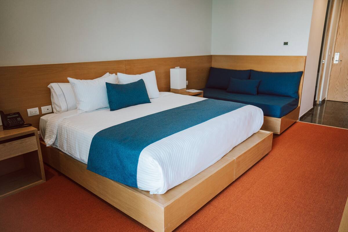 Een hotelkamer met een groot bed, een kleiner bed, een nachtkastje met een telefoon en een houten hoofdbord.