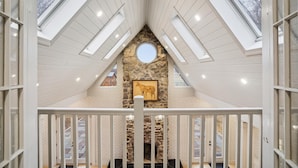 A spacious attic room with high ceilings, skylights, and a stone fireplace.