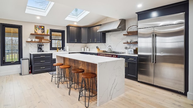 A modern kitchen with dark cabinets, a stainless steel refrigerator, and a central island with stools.