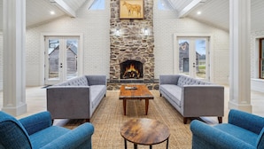 A spacious living room with a stone fireplace, two grey sofas, a coffee table, and a blue armchair.