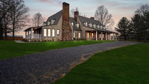 A large stone house with a prominent chimney, a covered porch, and a well-maintained lawn.