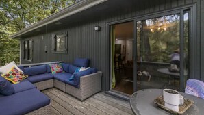 Eine moderne Holzhütte mit einer großen Schiebetür, einer überdachten Terrasse inklusive Sofa und Kissen sowie einem kleinen Tisch mit einem Blumentopf.