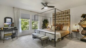 Ein Schlafzimmer mit einem Himmelbett, einem Schreibtisch mit Spiegel, einer kleinen Bank und einem Deckenventilator.