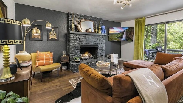 Ein modernes Wohnzimmer mit Kamin aus Stein, einer Ledersofa und einem an der Wand montierten Fernseher.