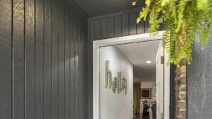 Ein moderner Eingangsbereich mit dunkler Holzfassade, einer Glastür und einer Fußmatte mit der Aufschrift 'HELLO'.