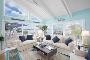 A spacious living room with a large window overlooking the beach, a white ceiling, and a view of the ocean.