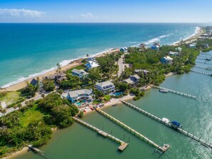 An aerial view of a coastal property with multiple buildings, a beach, and a pier extending into the water.