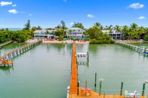 A waterfront property with a wooden dock leading to a docked boat, surrounded by lush greenery and a clear blue sky.