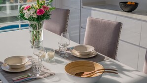 Een eettafel gedekt met witte borden, kommen en bestek, een vaas met bloemen en een kaars.