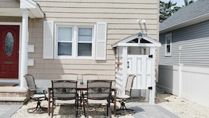 Een huis met een rode deur, witte luiken en een klein terras met een tafel en stoelen.