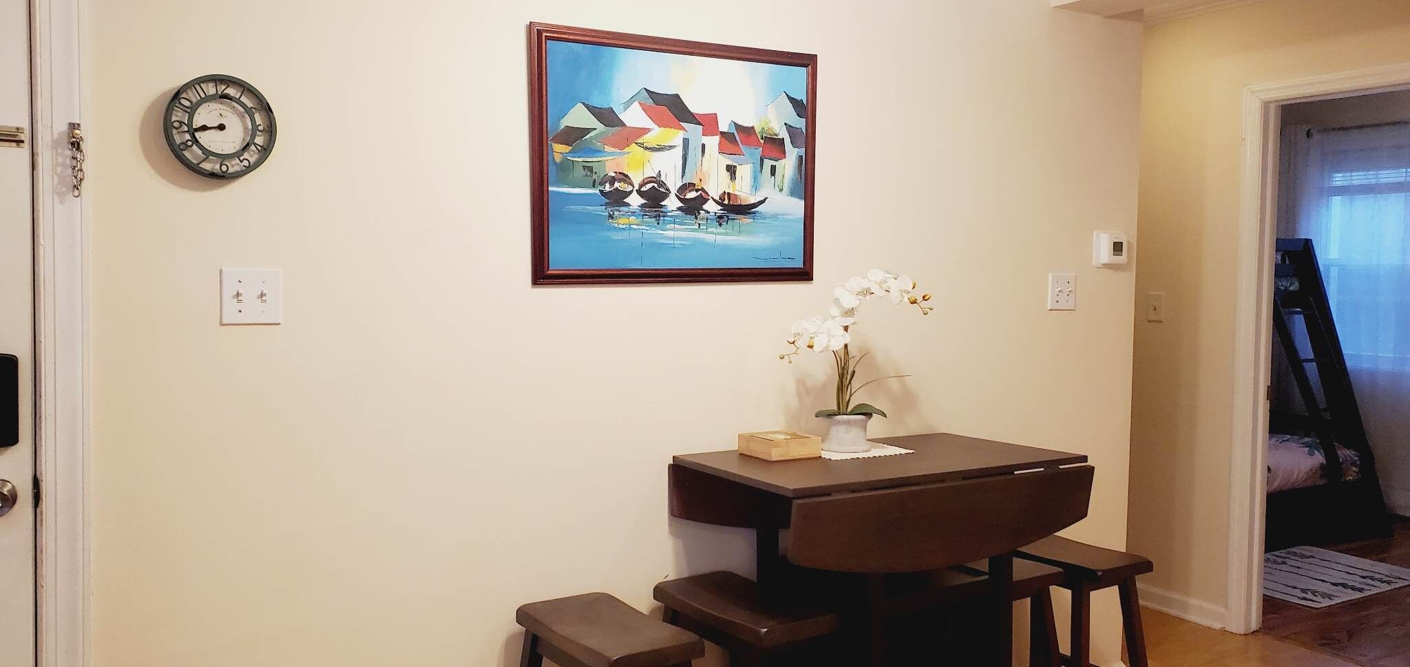 Un comedor con una mesa, sillas, un reloj y un cuadro en la pared.