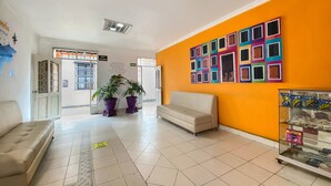 A lobby with a beige sofa, a white couch, potted plants, a colorful wall art, and a snack display. - Ayenda Republicano Colonial No 2 (Santa Marta)