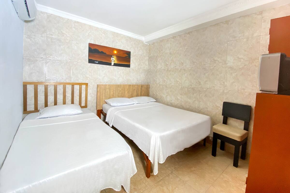A hotel room with two single beds, a wooden headboard, a small chair, a painting on the wall, and a tiled floor.
